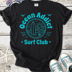 Black cotton t-shirt featuring 'Ocean Addict Surf Club' graphic in teal, perfect for beach lovers.