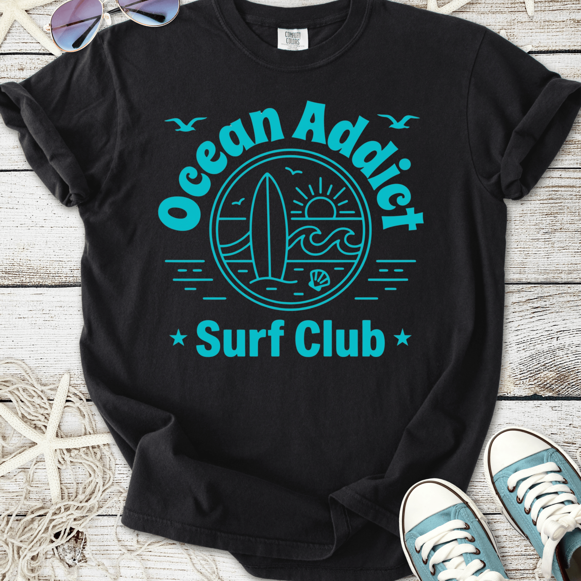 Black cotton t-shirt featuring 'Ocean Addict Surf Club' graphic in teal, perfect for beach lovers.