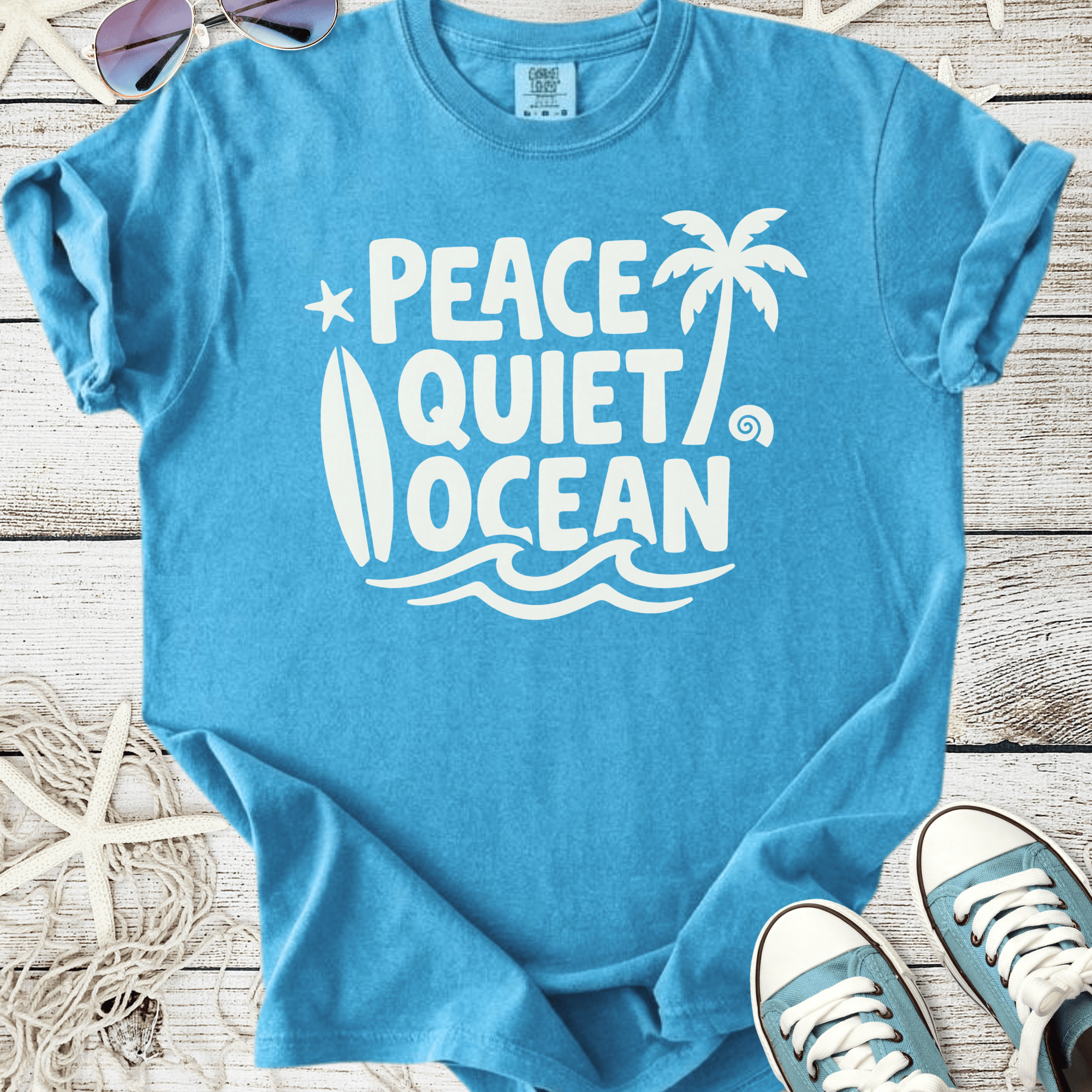 Light blue graphic t-shirt featuring 'Peace Quiet Ocean' design with surfboard and palm tree.