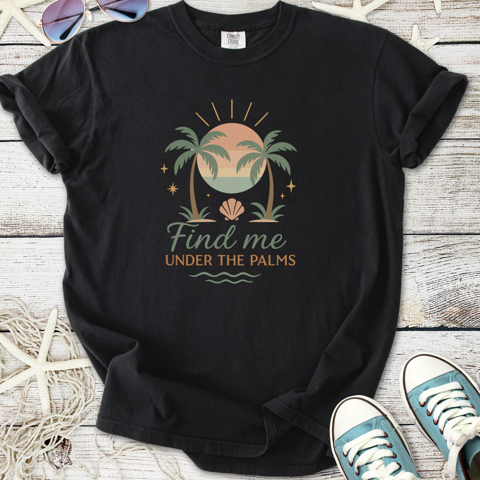 Black graphic t-shirt featuring 'Find me under the palms' with palm trees and sun design.