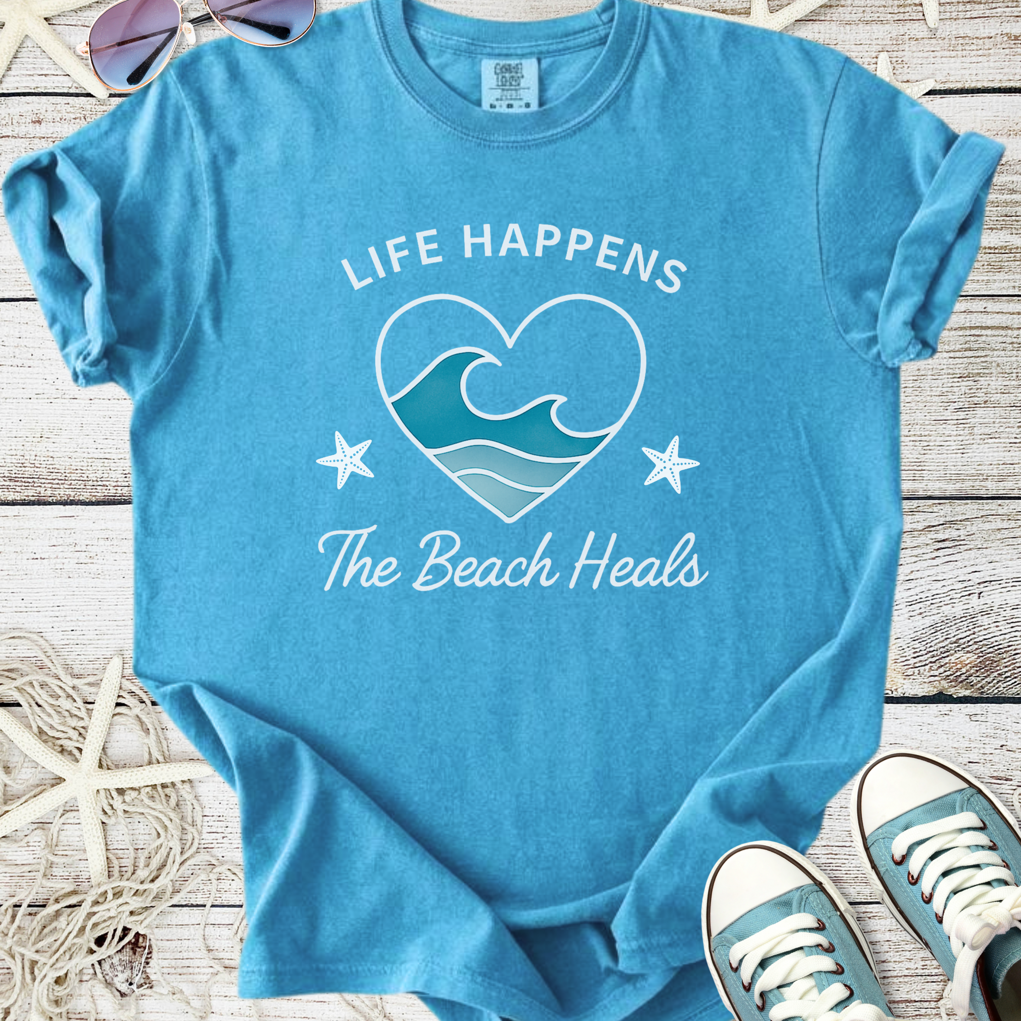 Blue cotton t-shirt with "Life Happens The Beach Heals" graphic, featuring waves and starfish design.