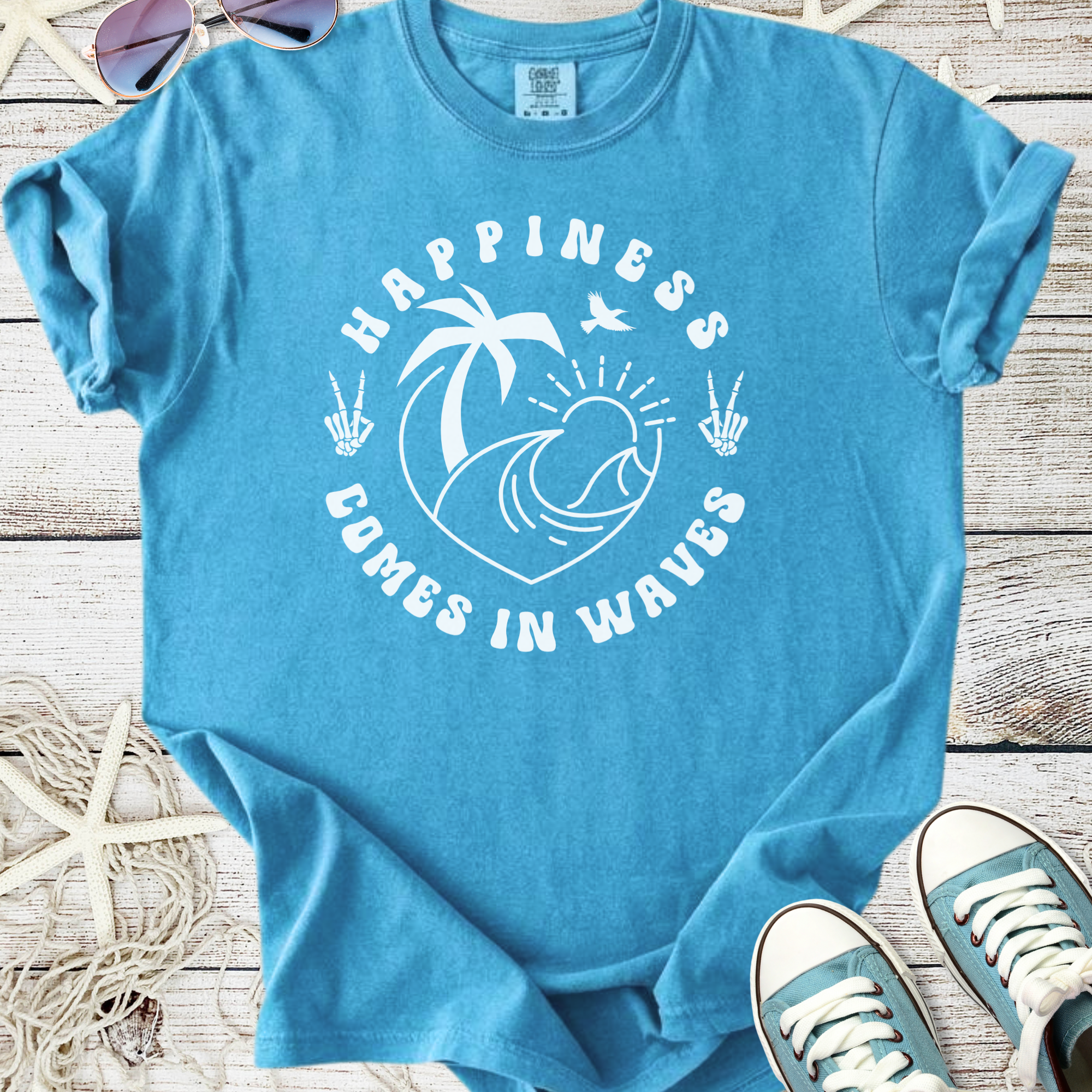 Light blue t-shirt with 'Happiness Comes in Waves' graphic, featuring palm trees and ocean waves.