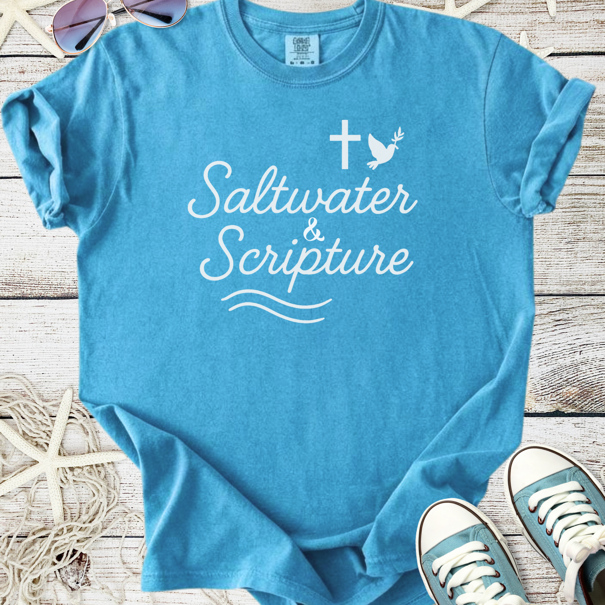Light blue t-shirt with 'Saltwater & Scripture' graphic, casual style for beach lovers.