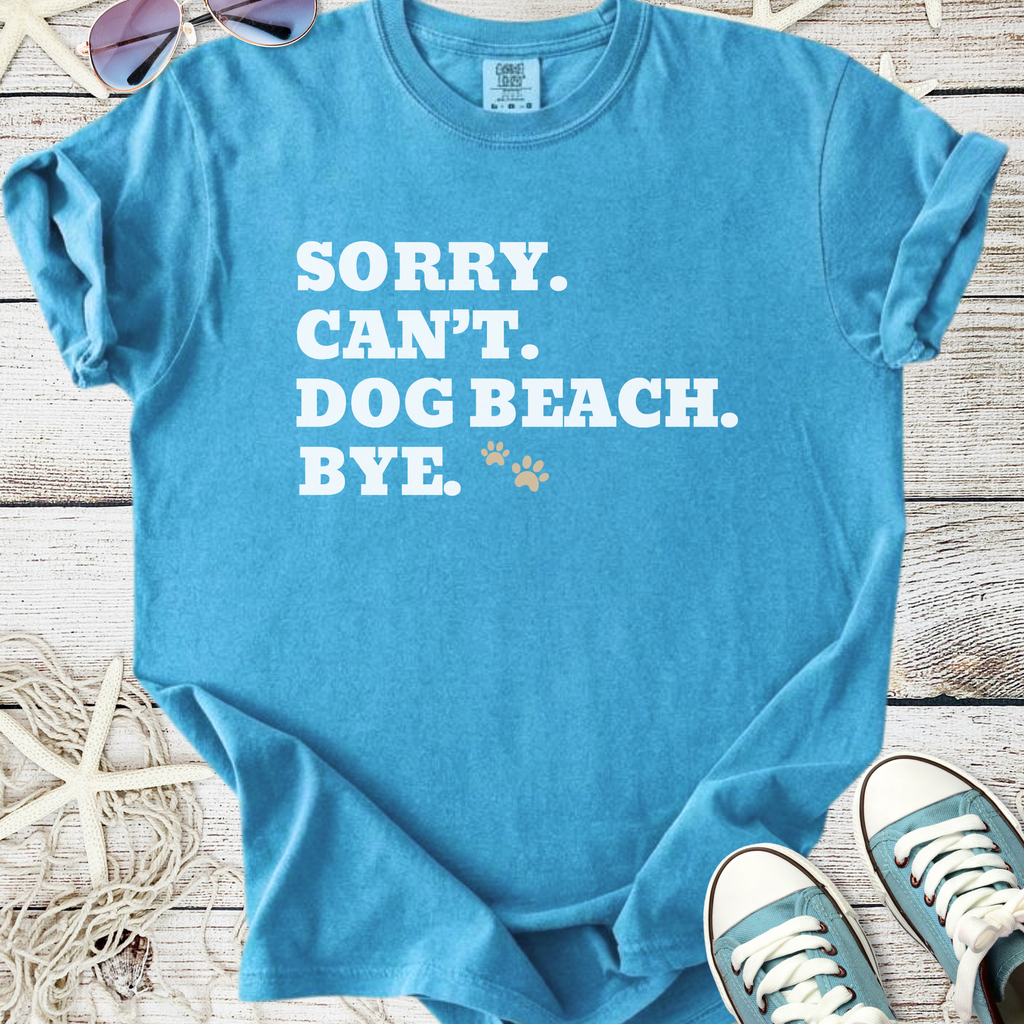 Light blue graphic tee with 'Sorry. Can't. Dog Beach. Bye.' text and paw prints. Perfect for dog lovers.