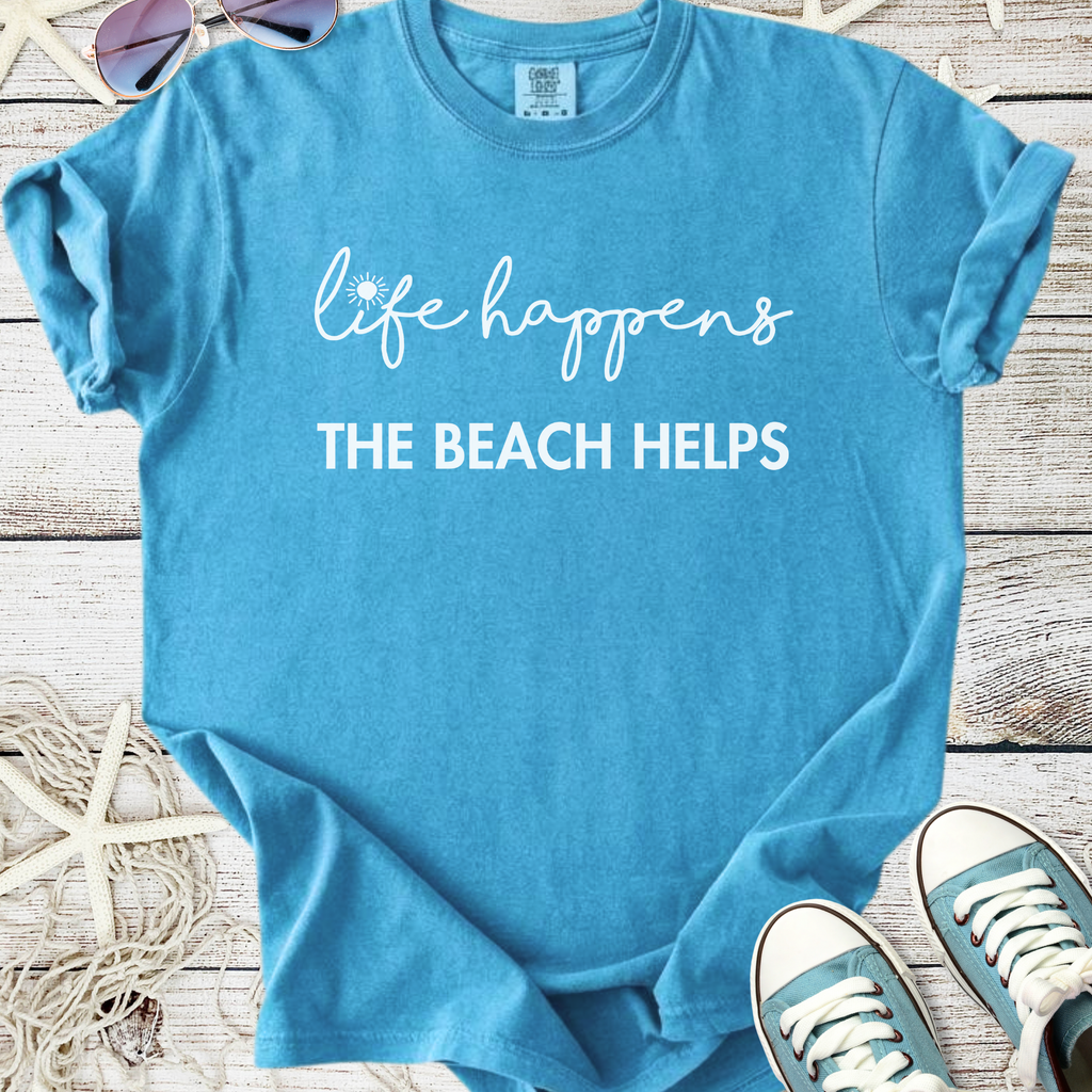 Light blue t-shirt with "life happens THE BEACH HELPS" printed, perfect for beach lovers and summer wear.