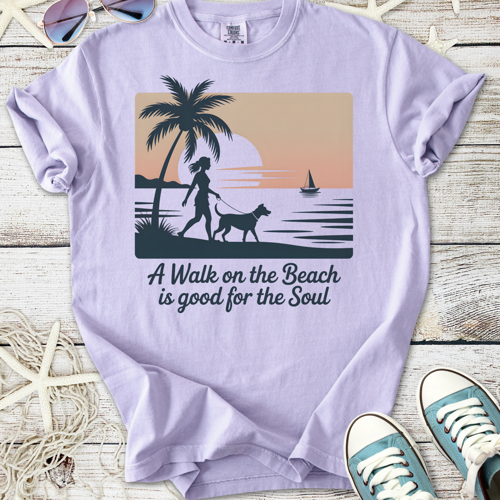 Light purple graphic t-shirt featuring a beach scene with a woman walking a dog, inspiring text.