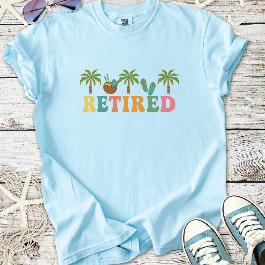 Light blue retired graphic t-shirt with palm trees and colorful text design, perfect for casual wear.