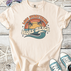 Cream-colored t-shirt with 'Less Everything, More Beach' graphic, featuring palm trees and waves.