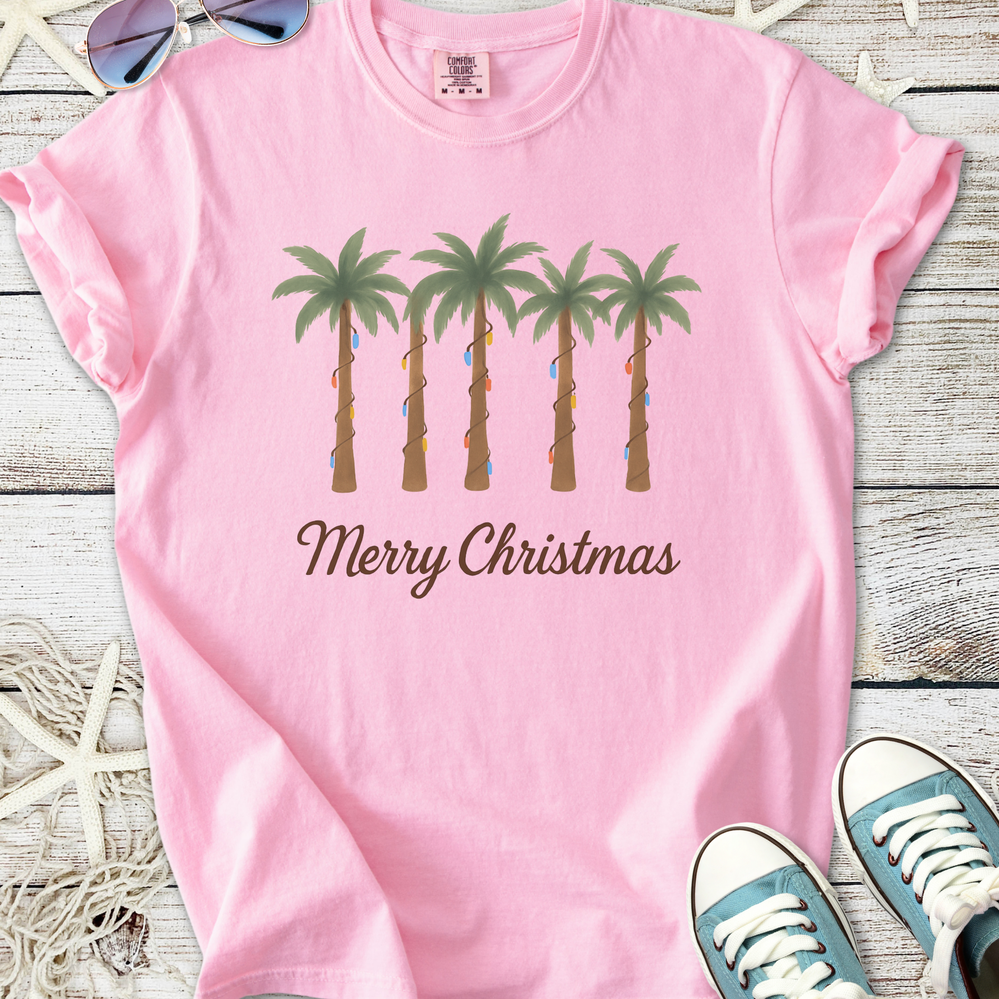 Pink Christmas t-shirt with palm tree design and 'Merry Christmas' text, perfect for festive beach vibes.