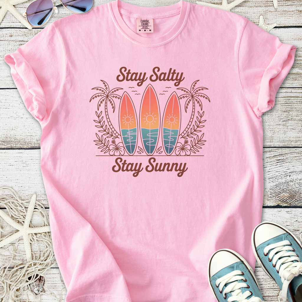 Pink beach themed graphic t-shirt with surfboards, palm trees, and ‘Stay Salty Stay Sunny’ text