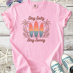 Pink beach themed graphic t-shirt with surfboards, palm trees, and ‘Stay Salty Stay Sunny’ text