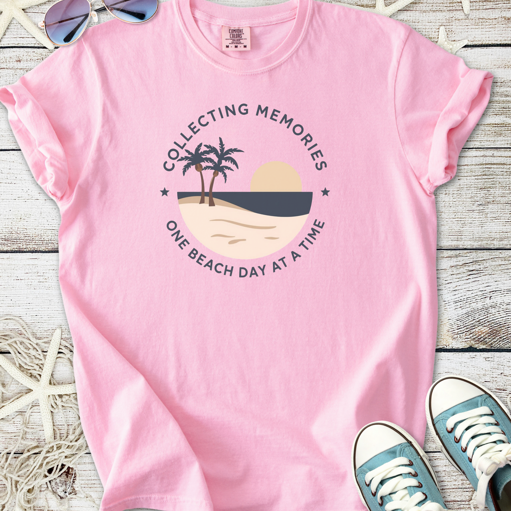 Pink graphic t-shirt with beach scene design, featuring palm trees and sunset, perfect for summer wear.