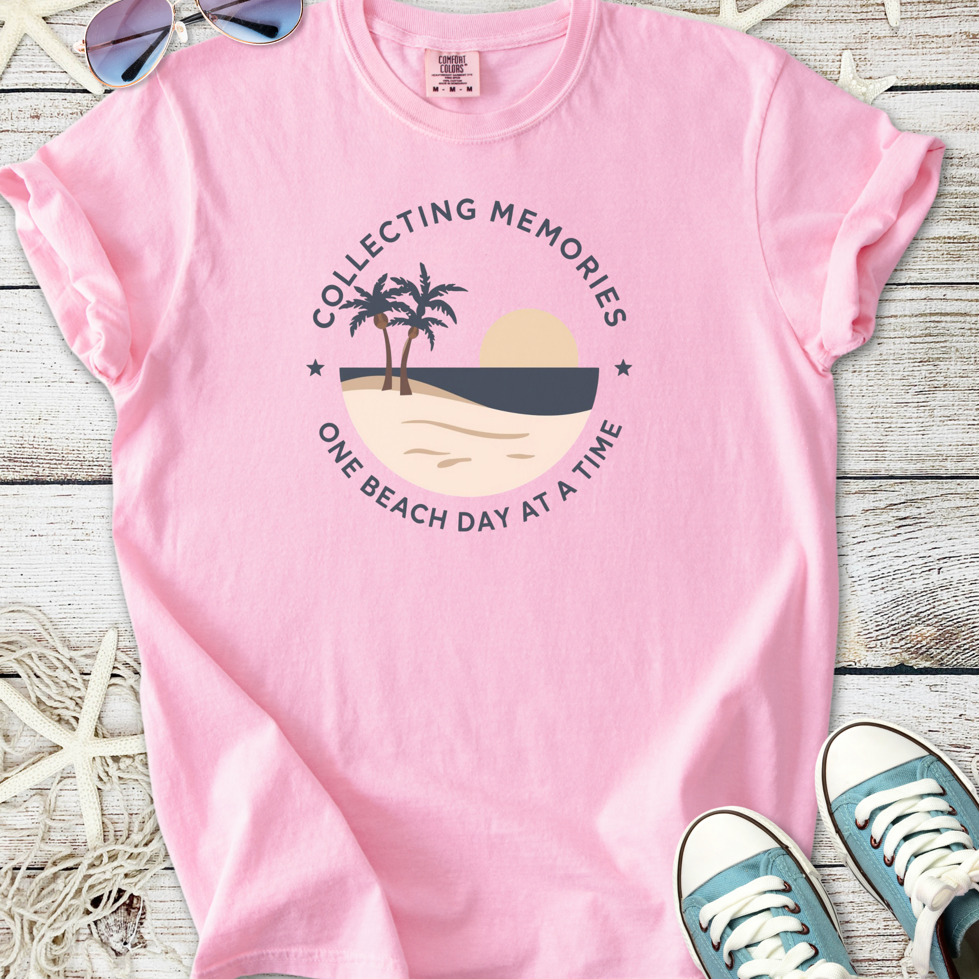 Pink graphic t-shirt with beach scene design, featuring palm trees and sunset, perfect for summer wear.