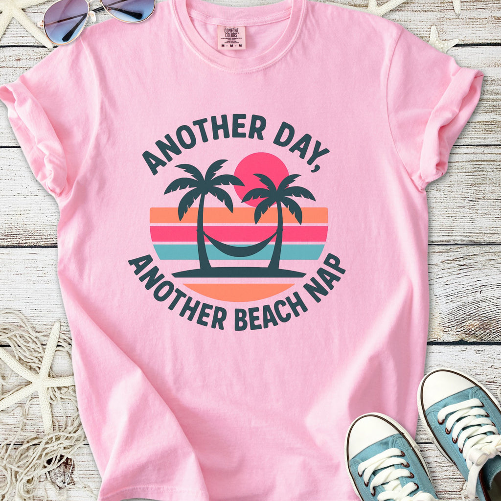Pink graphic t-shirt featuring palm trees and 'Another Day, Another Beach Nap' text, made from soft cotton.