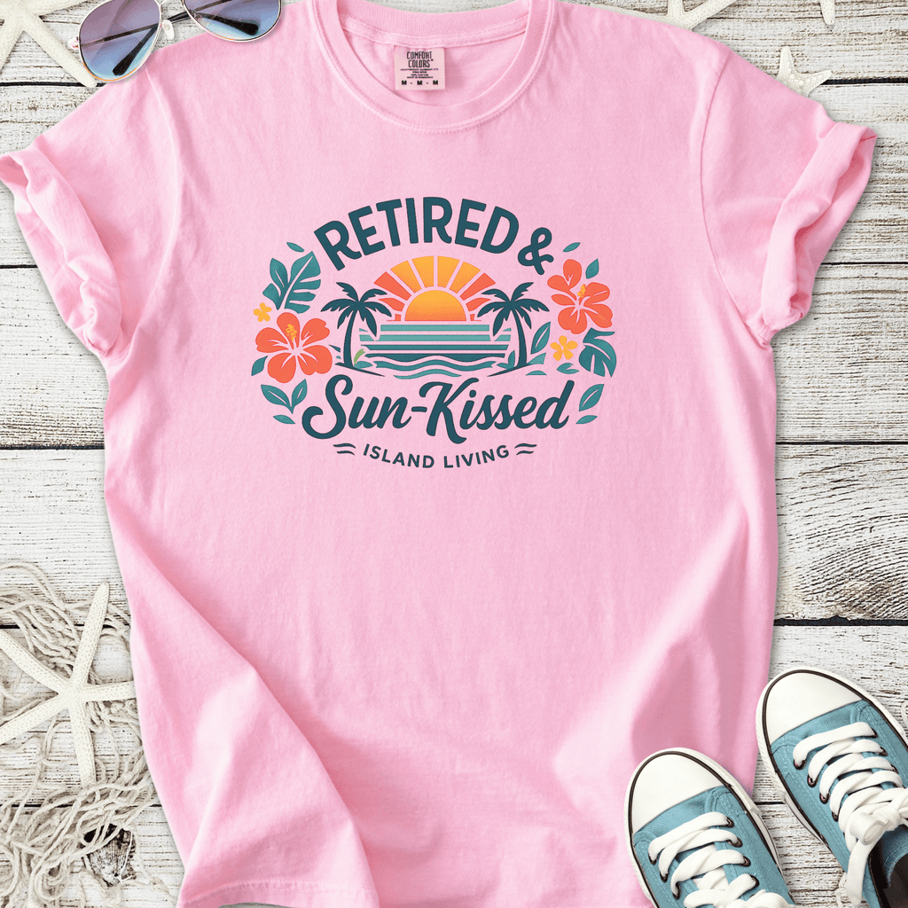 Pink t-shirt featuring 'Retired & Sun-Kissed' graphic with tropical design, perfect for island living.