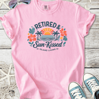 Pink t-shirt featuring 'Retired & Sun-Kissed' graphic with tropical design, perfect for island living.