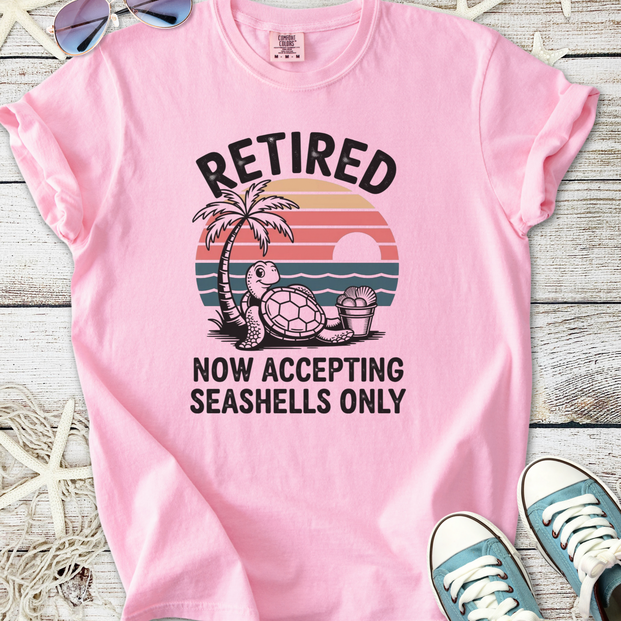 Pink retired tee with turtle graphic, palm tree, and text 'Now Accepting Seashells Only'.