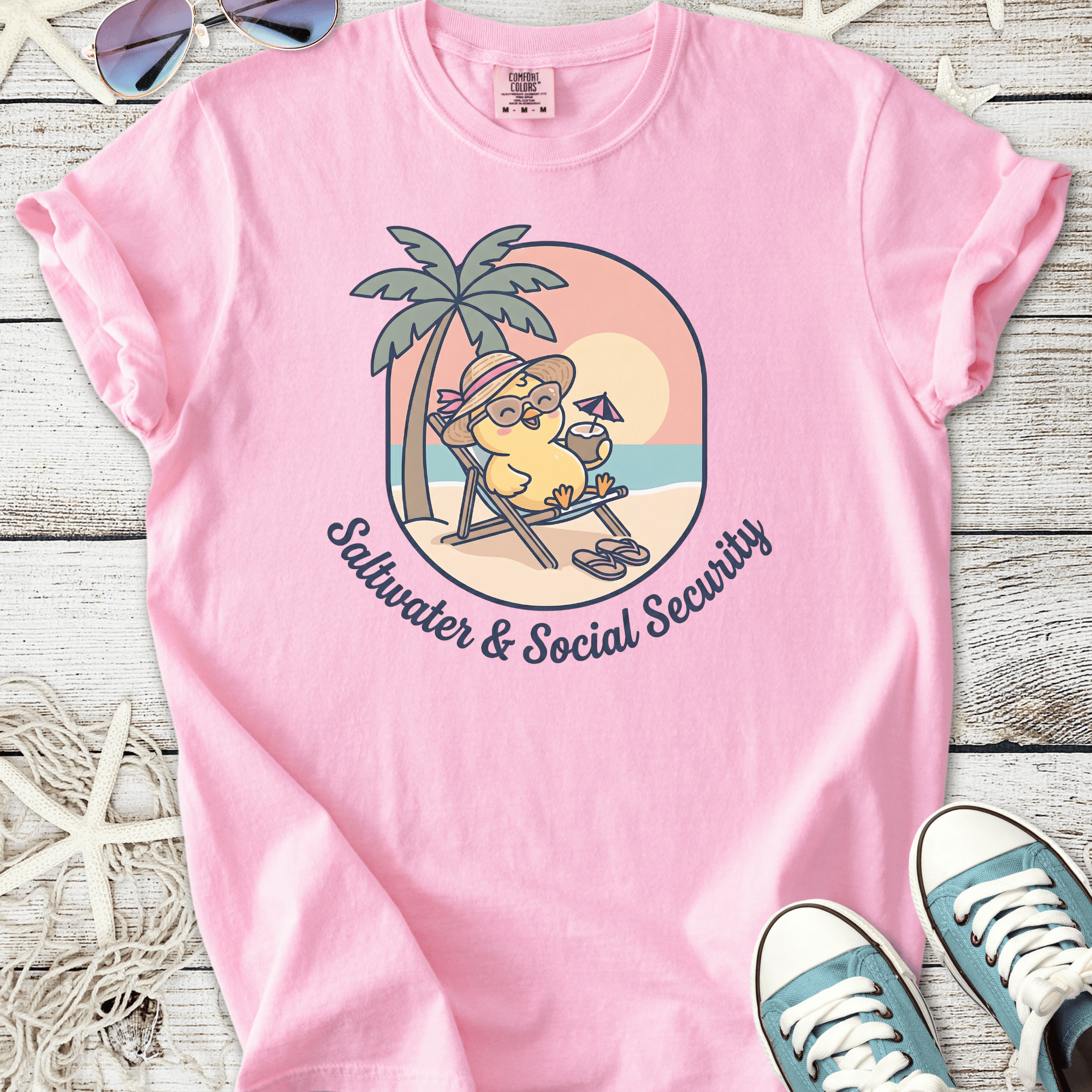 Pink cotton t-shirt with 'Saltwater & Social Security' graphic featuring a cartoon character relaxing on a beach.