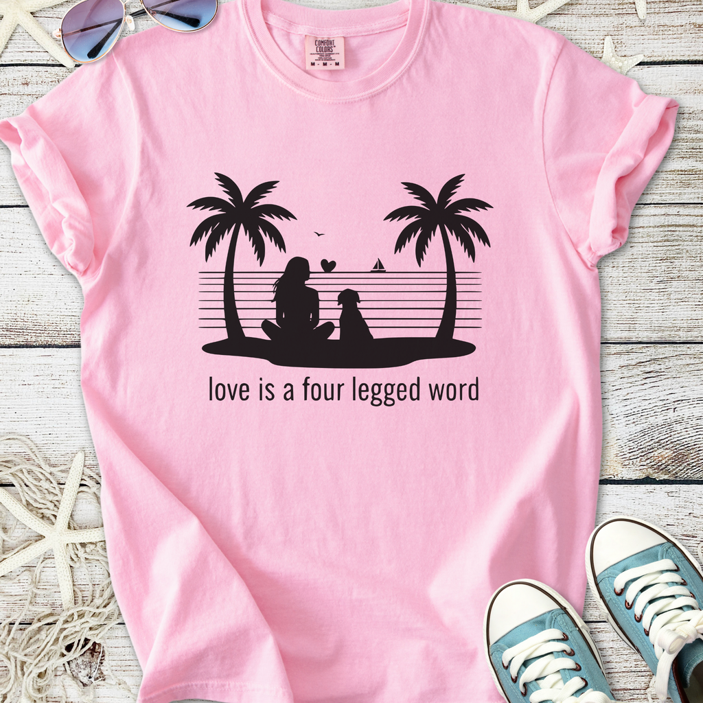 Pink beach themed dog lover graphic t-shirt with palm trees, woman and dog silhouette, and ‘Love is a four legged word’ text