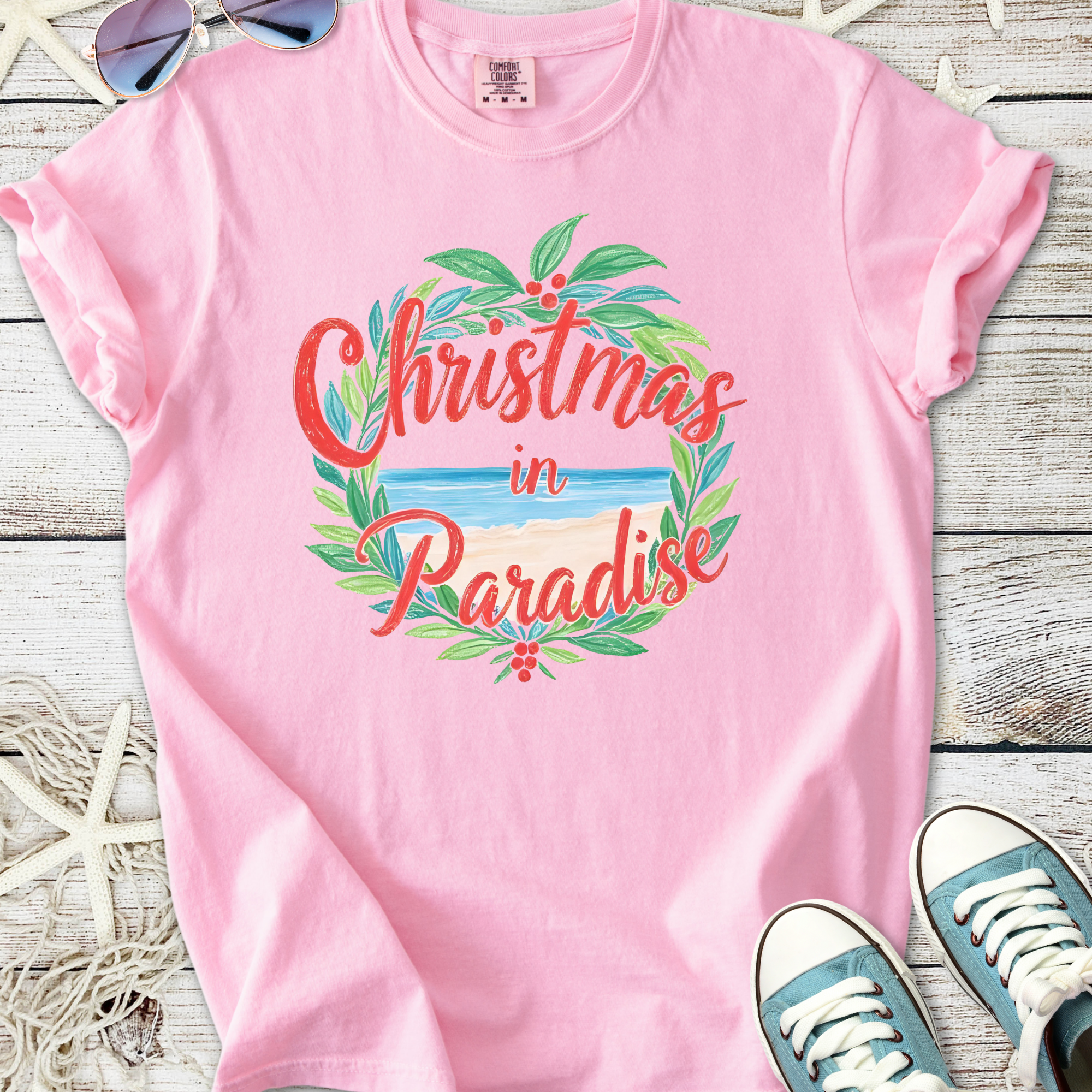 Light pink t-shirt featuring a 'Christmas in Paradise' graphic with beach and foliage design.
