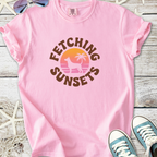 Pink cotton t-shirt featuring 'Fetching Sunsets' graphic with a palm tree and dog silhouette.