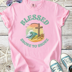 Pink graphic t-shirt featuring 'Blessed Shore to Shore' design with wave and cross illustration.