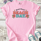 Pink graphic tee with 'Bad Day? Beach Day' print, floral design, perfect for casual summer wear.