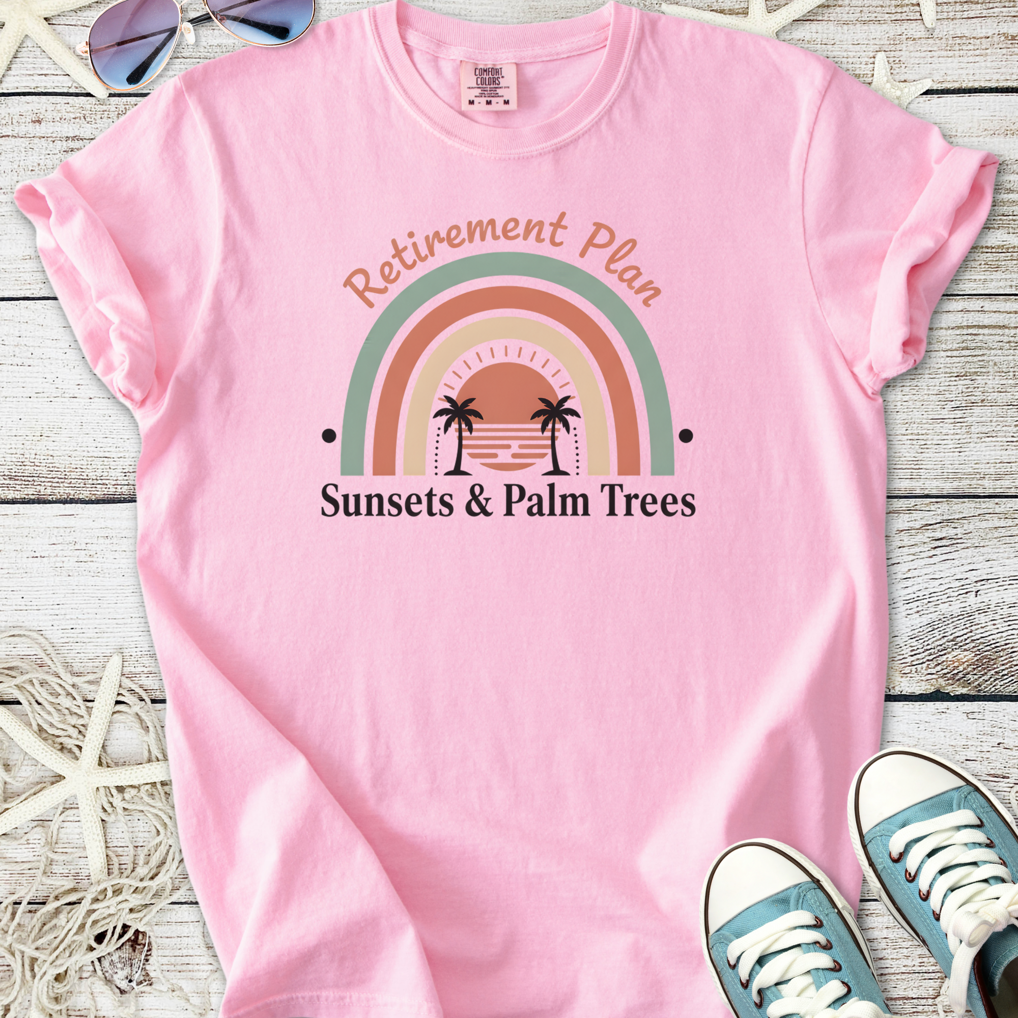 Pink cotton t-shirt with 'Retirement Plan' and sunset graphic featuring palm trees.