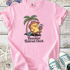 Pink t-shirt featuring a cute chick relaxing with drinks under a palm tree, perfect for beach lovers.