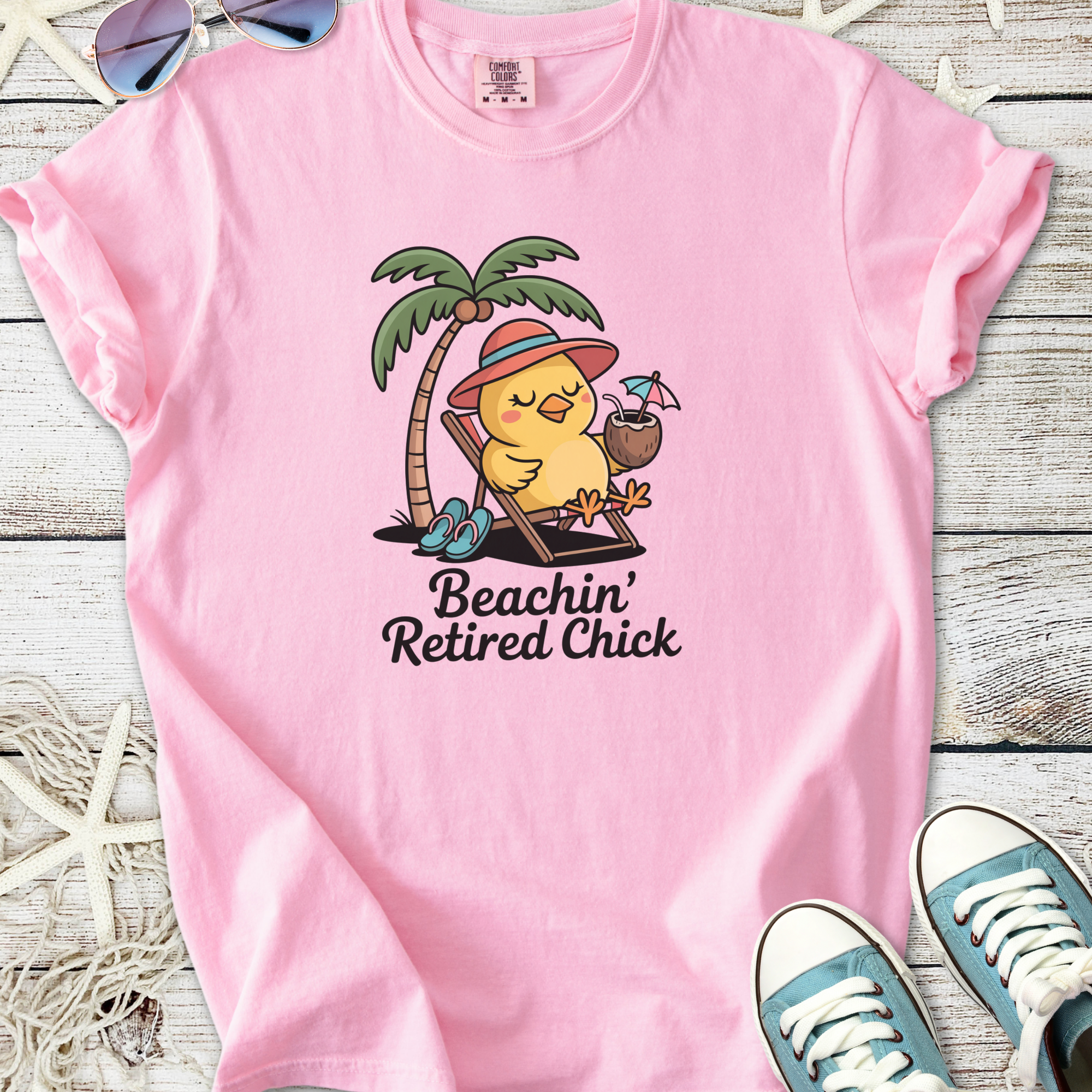 Pink t-shirt featuring a cute chick relaxing with drinks under a palm tree, perfect for beach lovers.