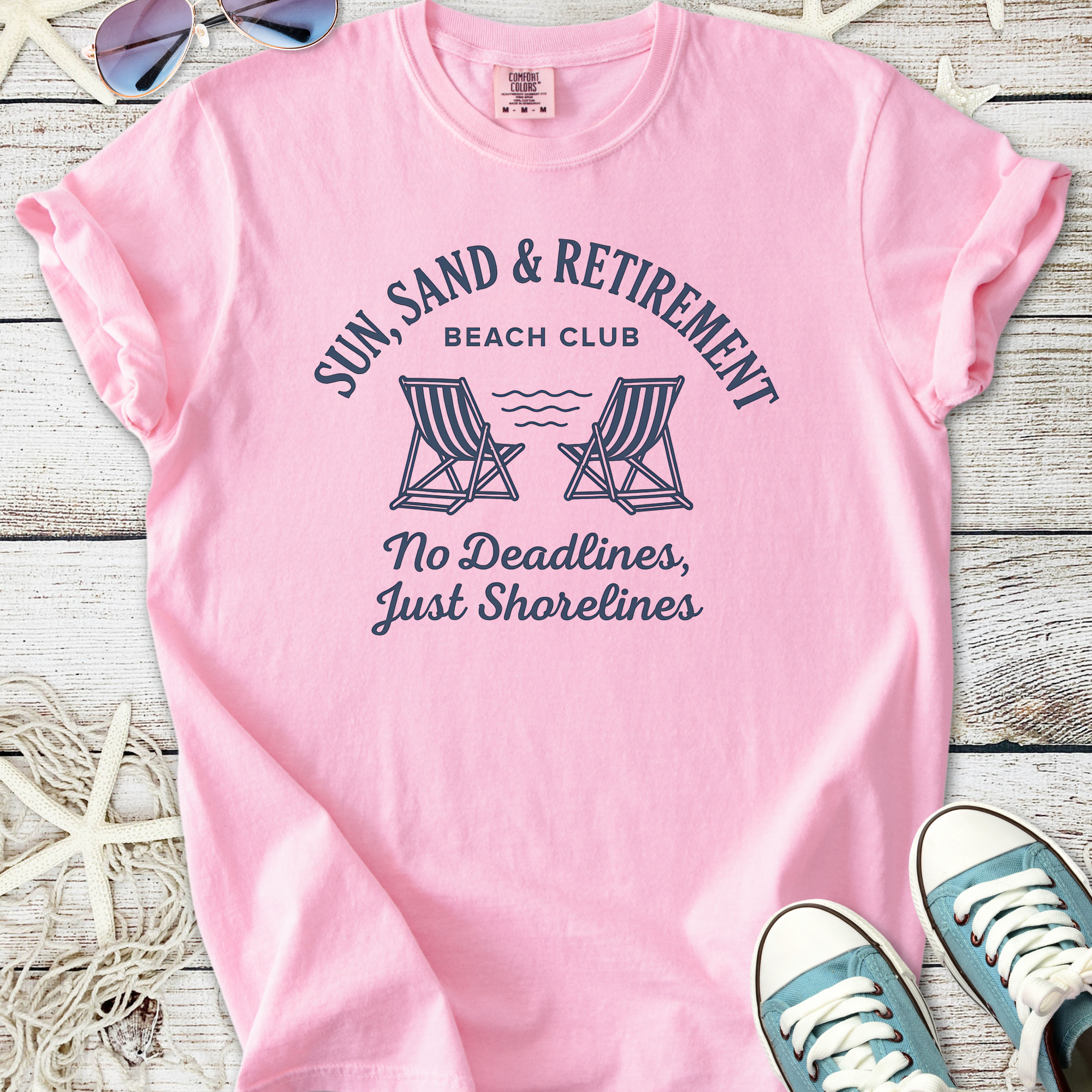 Pink cotton t-shirt with 'Sun, Sand & Retirement' graphic, perfect for beach lovers.