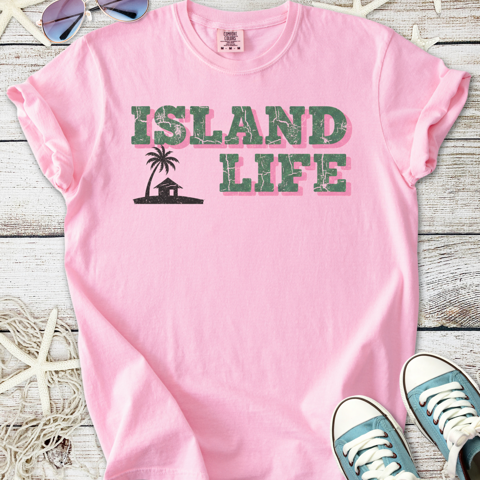 Pink cotton t-shirt featuring 'Island Life' print with palm tree and house design.