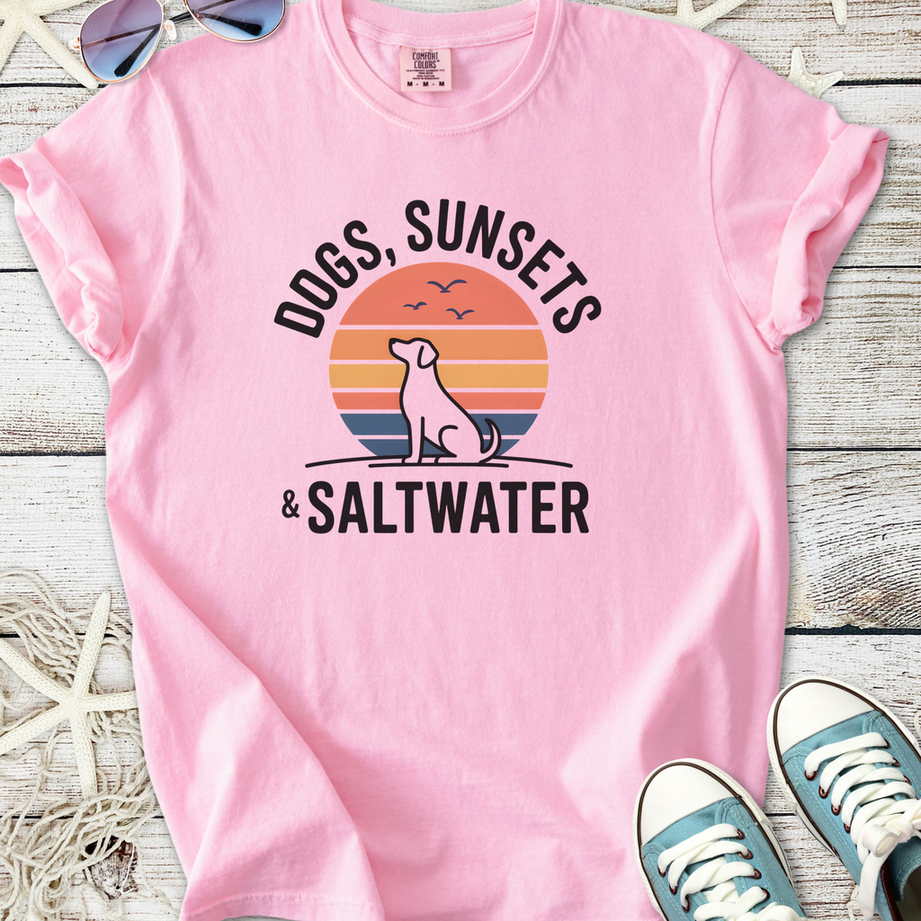 Pink graphic tee featuring 'Dogs, Sunsets & Saltwater' design, great for beach lovers and dog enthusiasts.