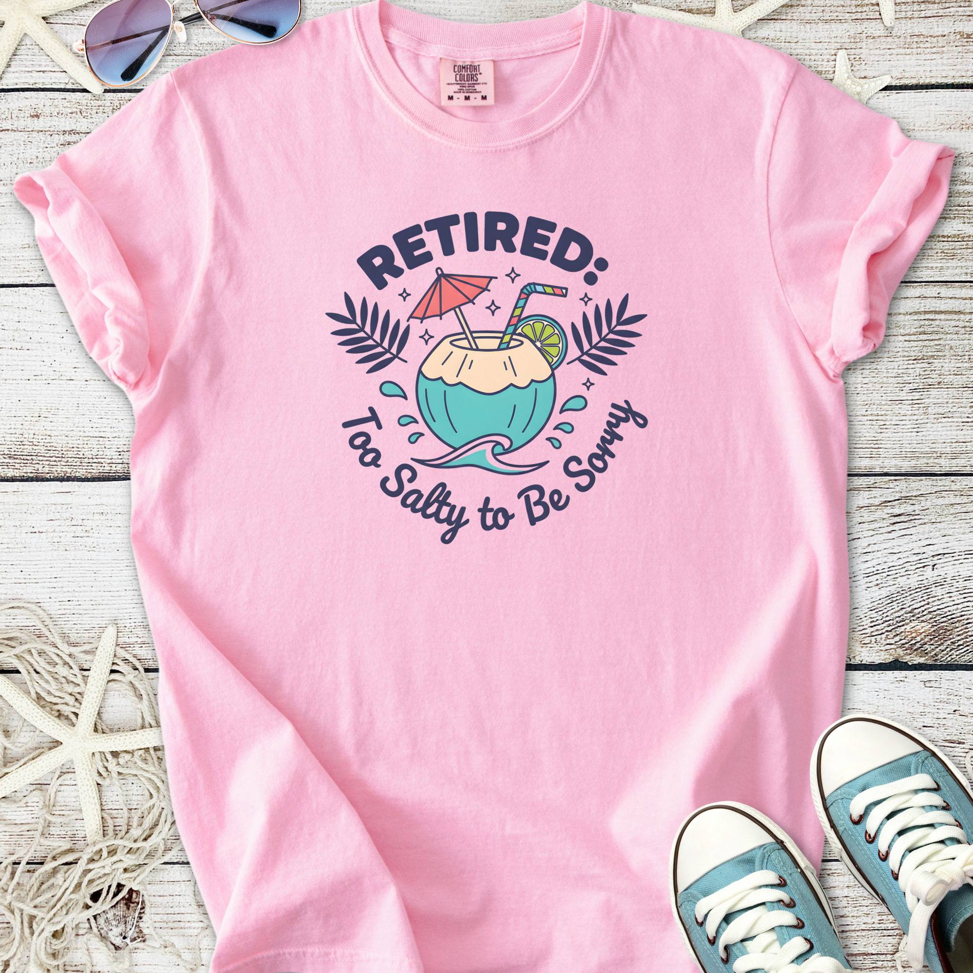 Pink cotton t-shirt with 'Retired: Too Salty to Be Sorry' graphic and tropical drink design.