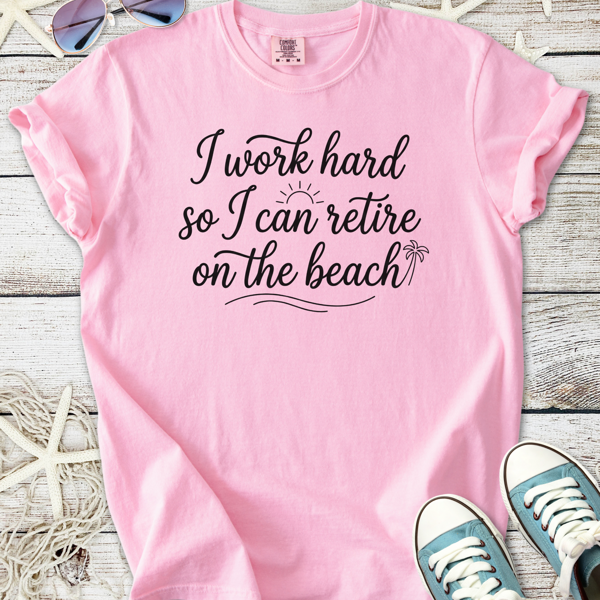 Pink t-shirt with the quote 'I work hard so I can retire on the beach', cotton material, casual style.