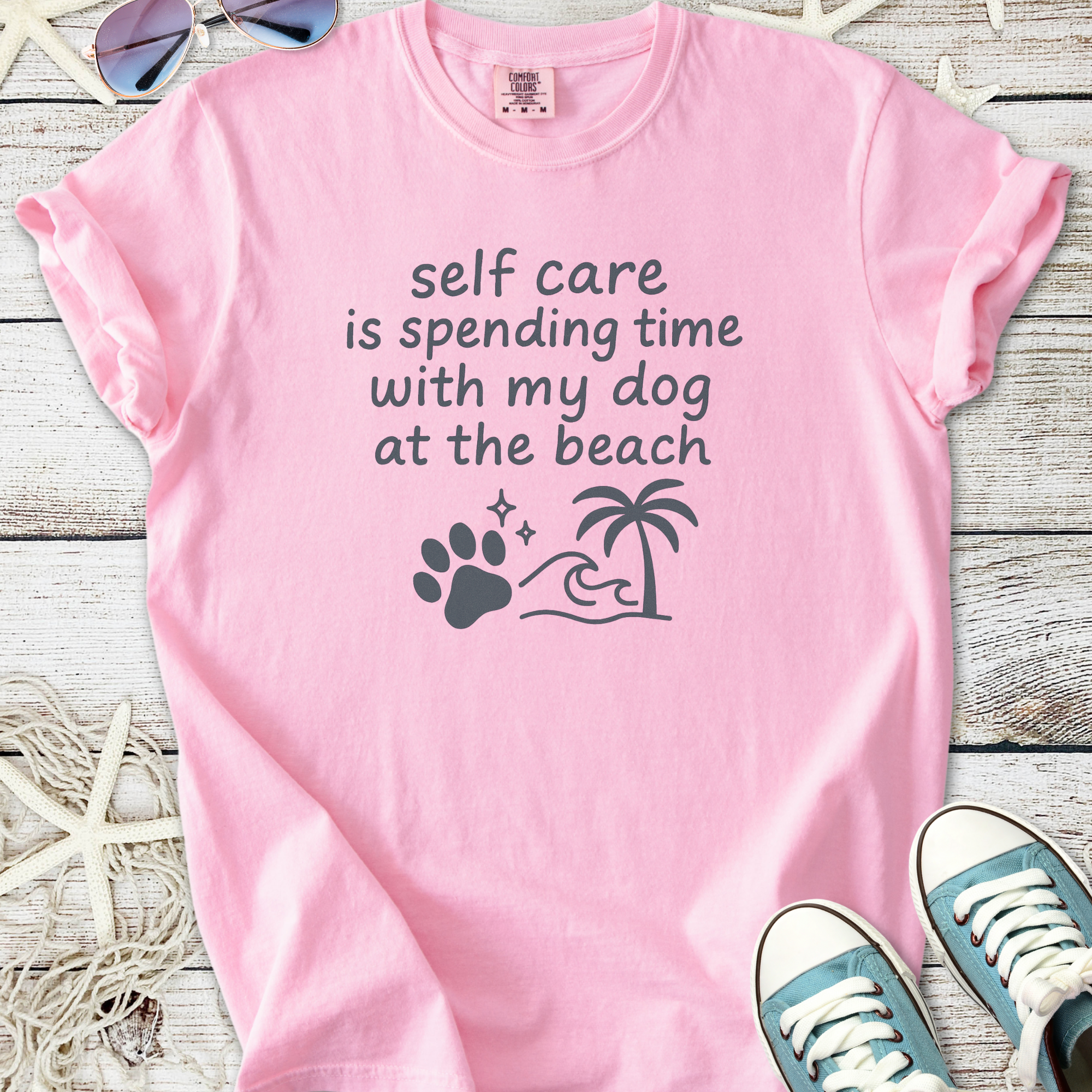 Light pink t-shirt with 'self care is spending time with my dog at the beach' graphic design.