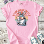 Pink t-shirt featuring a cute dolphin with bunny ears and heart-shaped sunglasses, ideal for beach lovers.