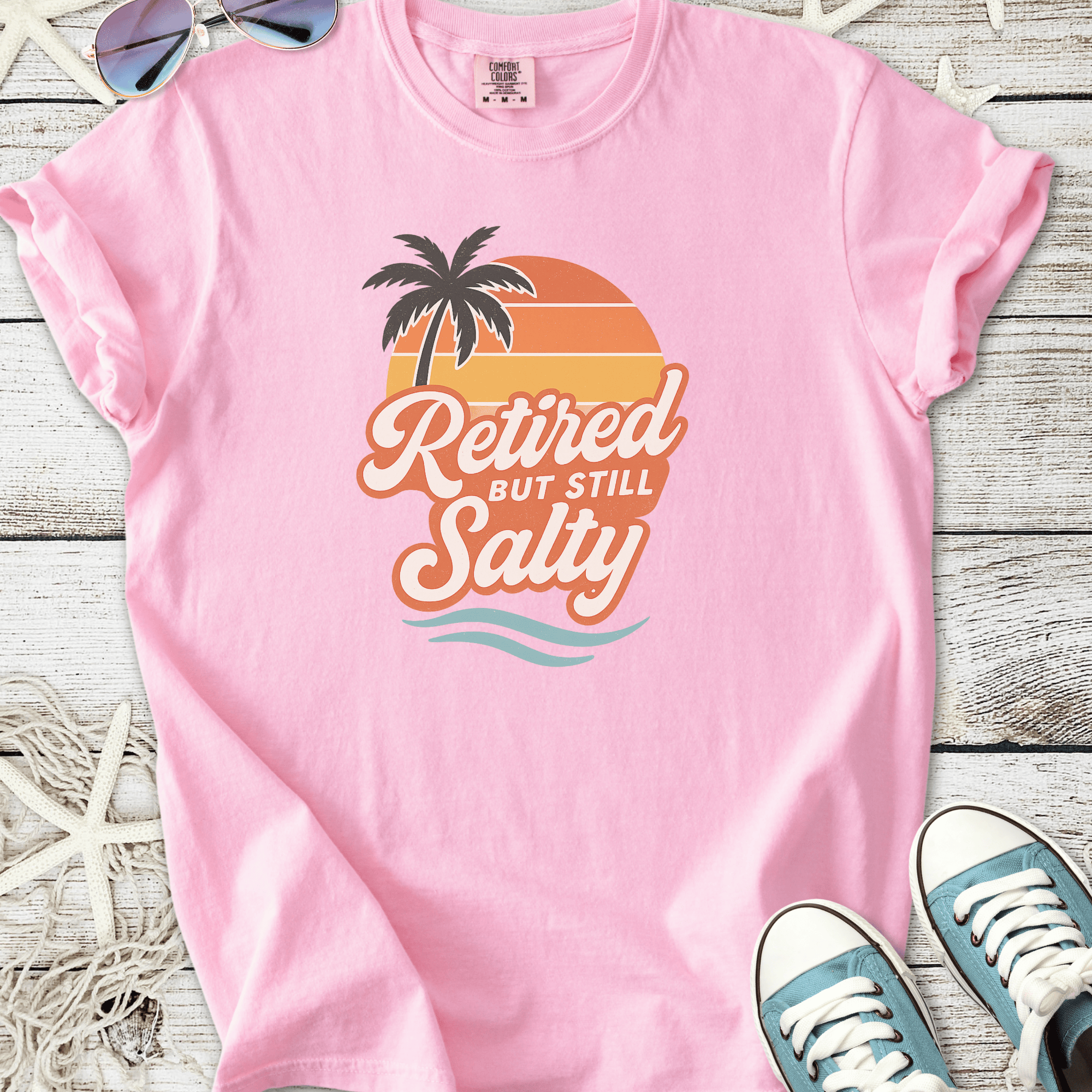 Pink graphic tee featuring 'Retired but still Salty' design with palm tree and sunset.