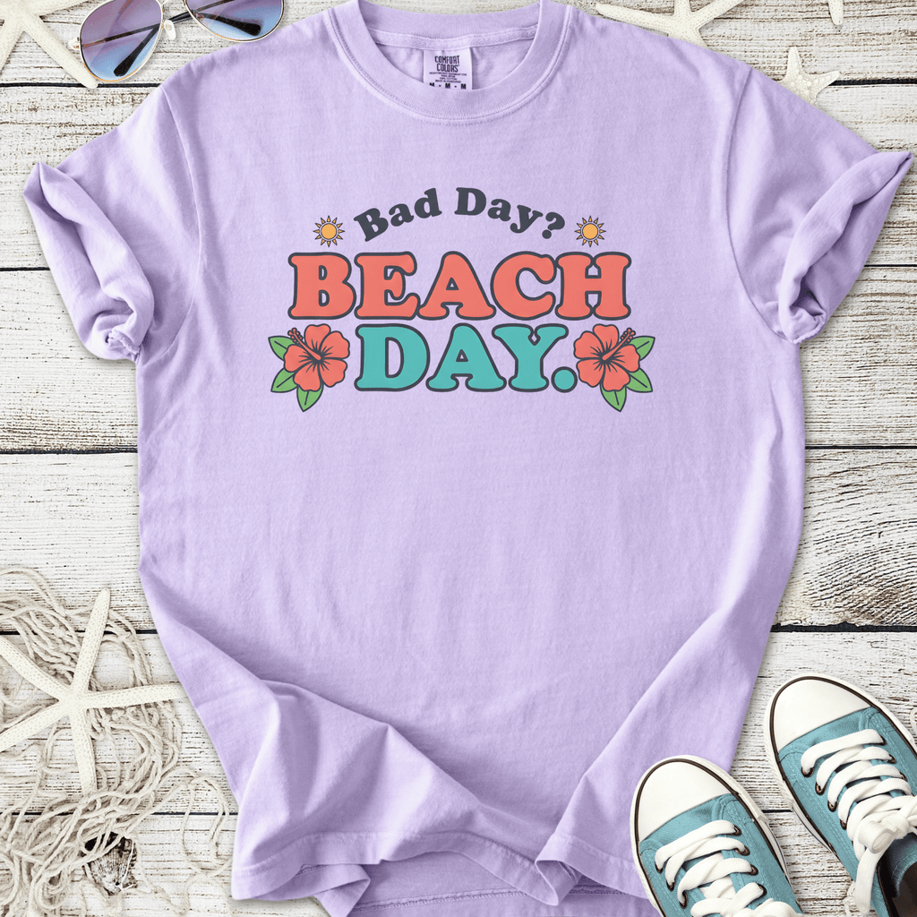 Lavender graphic t-shirt with 'Bad Day? BEACH DAY.' text and floral design, perfect for summer wear.