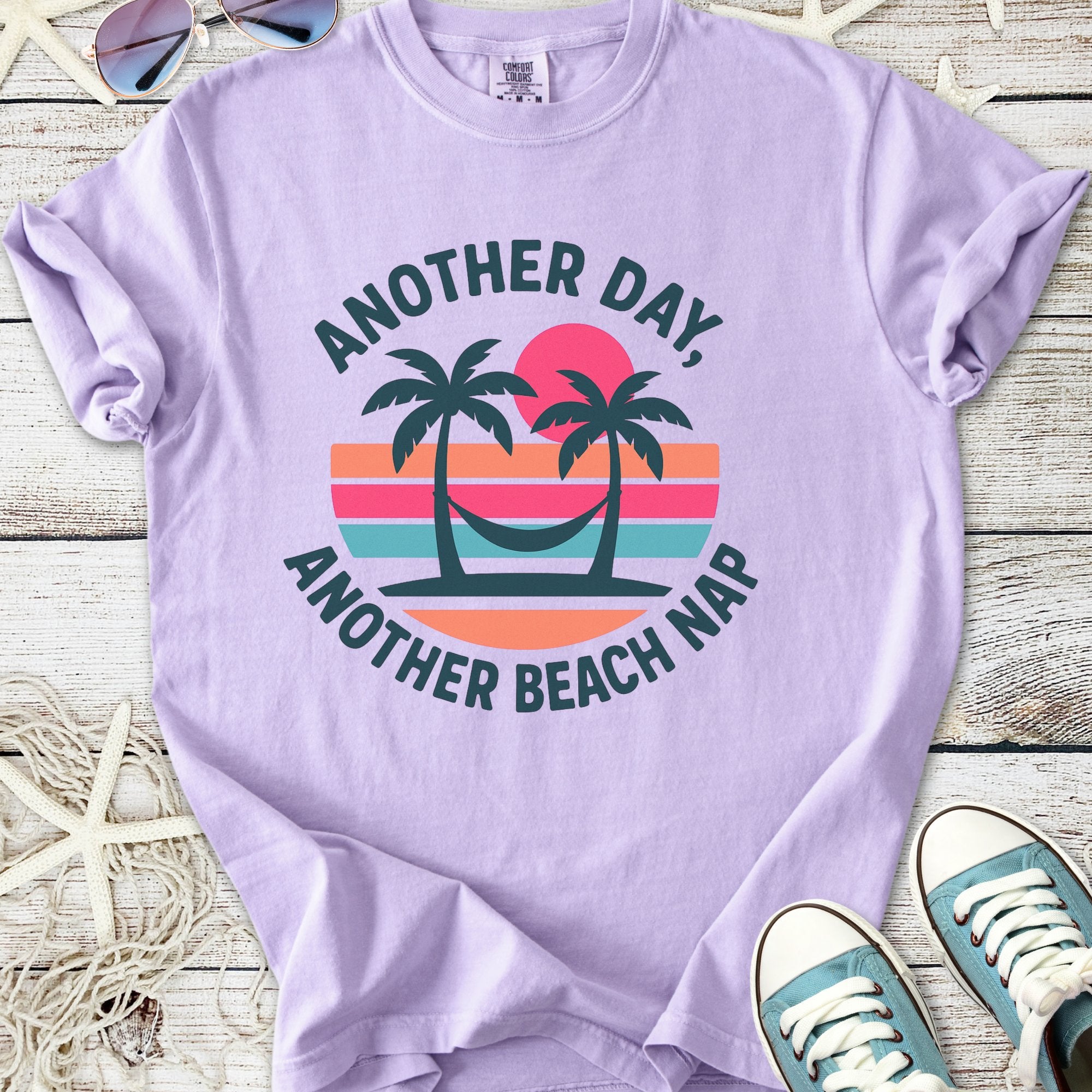 Light purple graphic t-shirt with 'Another Day, Another Beach Nap' text and palm tree design.