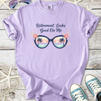 Light purple t-shirt with 'Retirement Looks Good On Me' graphic featuring sunglasses and tropical design.