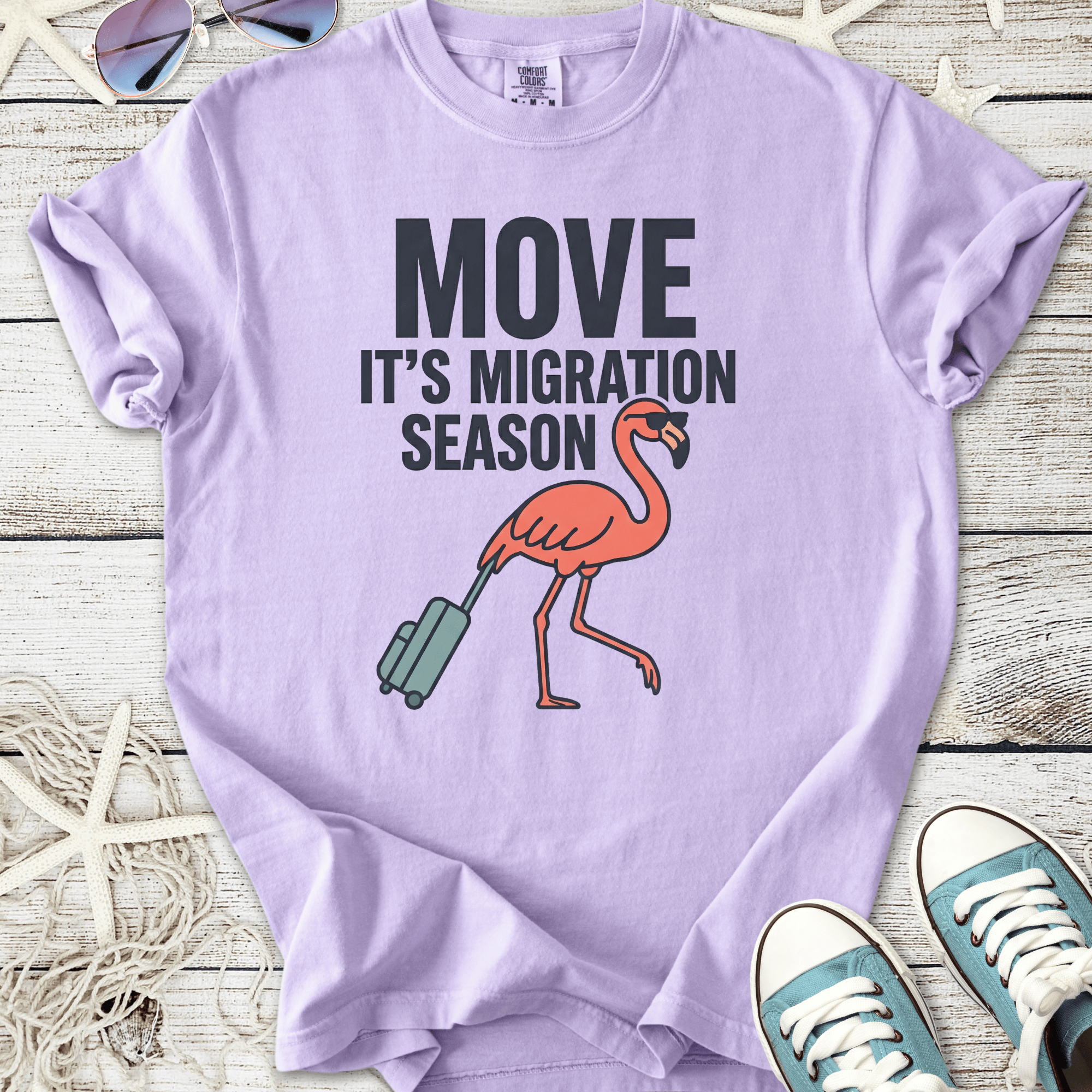 Lilac t-shirt with 'MOVE IT'S MIGRATION SEASON' and a flamingo graphic, perfect for casual wear.