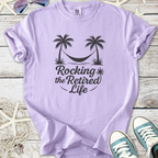 Lavender t-shirt with 'Rocking the Retired Life' print, featuring palm trees and a hammock, casual style.