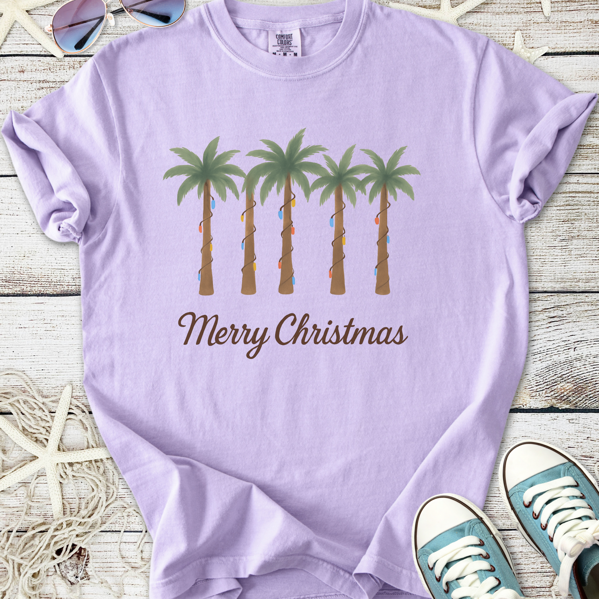 Lilac t-shirt with Christmas palm trees design, featuring festive lights and 'Merry Christmas' text.