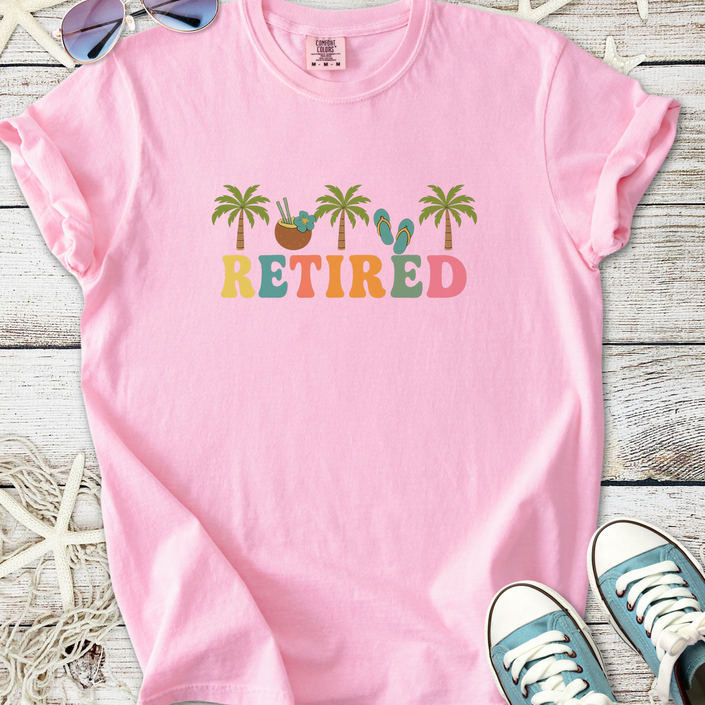 Light pink t-shirt with 'RETired' graphic, featuring palm trees and flip flops, perfect for casual wear.