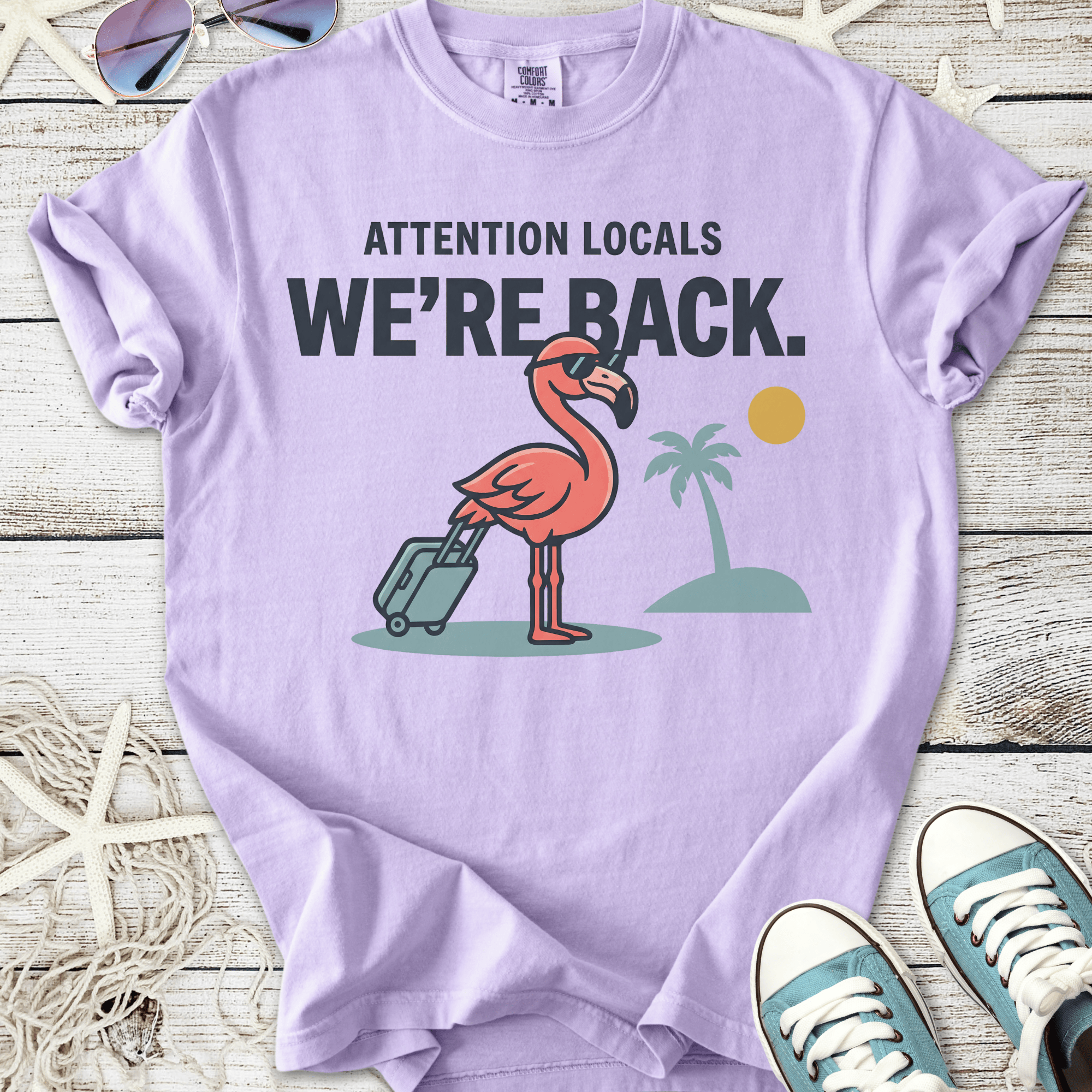 Purple t-shirt with a flamingo graphic, featuring suitcase and palm trees, perfect for summer vibes.