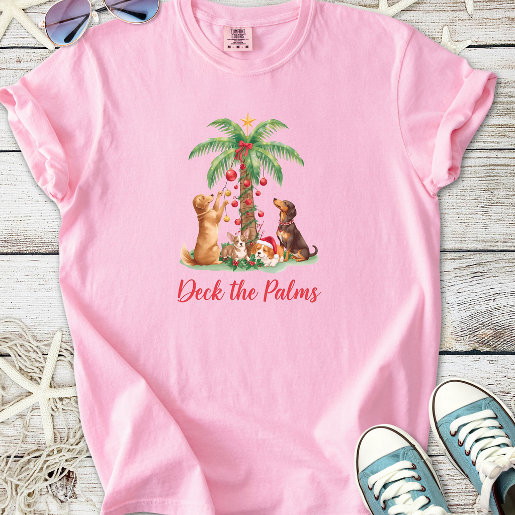 Pink t-shirt featuring playful dogs decorating a palm tree with Christmas ornaments. Cute and festive design.