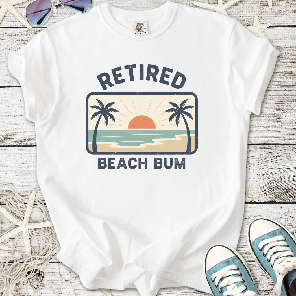 White t-shirt with 'Retired Beach Bum' graphic, featuring palm trees and sunset design, perfect for casual summer wear.