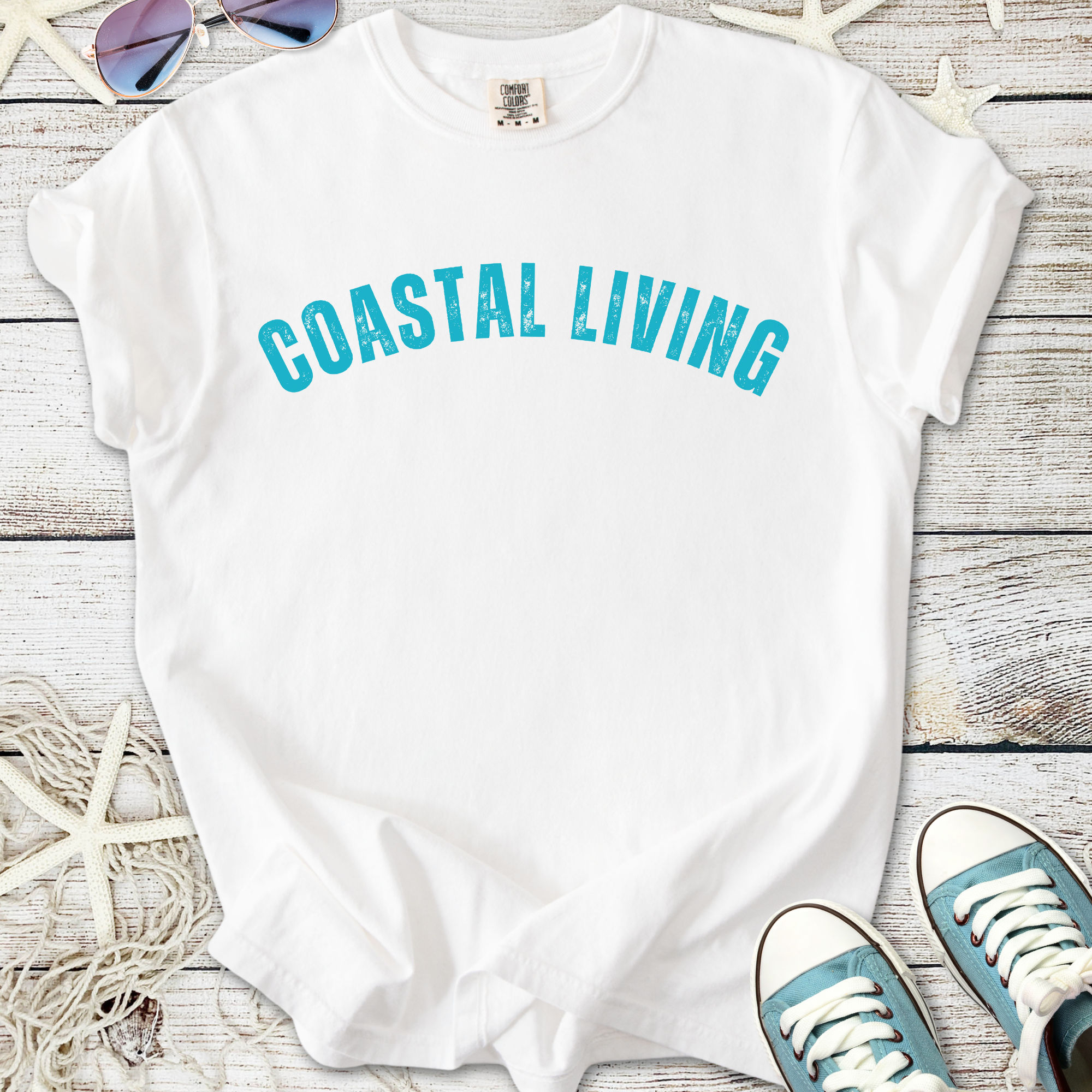 White t-shirt featuring 'Coastal Living' print in teal, perfect for beach lovers and casual wear.