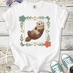 Cute white t-shirt featuring an illustrated otter surrounded by floral designs, perfect for casual wear.
